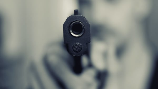 A pistol pointed at the point of view, with the blurry image of the gun holder behind it.